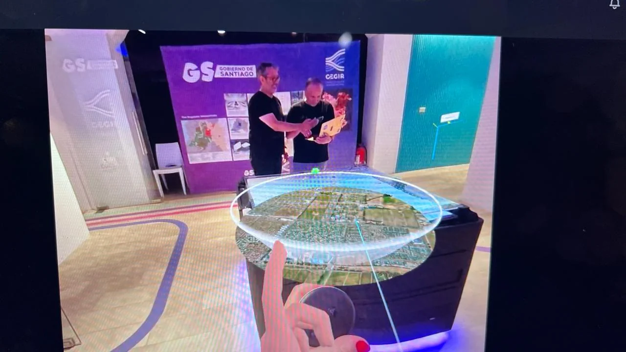 First-person VR view: a holographic disc shows an aerial crop of a Santiago residential grid while two CEGIR staff demo a tablet in the background.