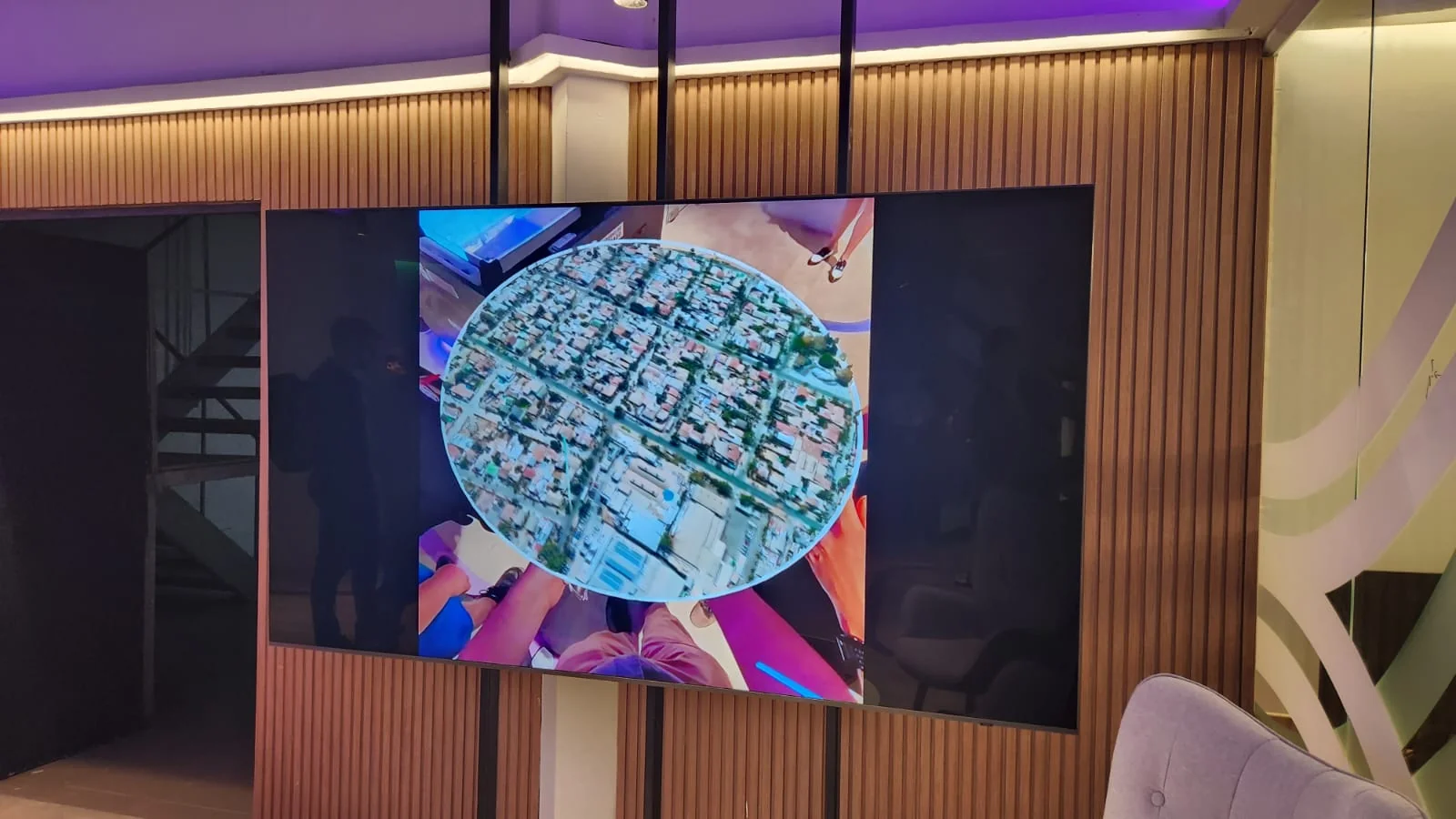 Wall screen mirroring the VR viewpoint: a circular satellite-imagery lens floats over a dark stage revealing a Santiago neighborhood block.