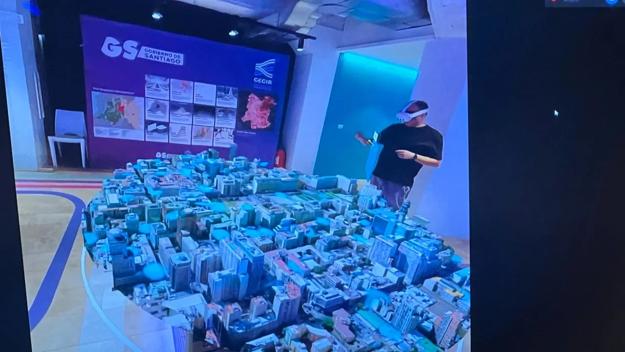 A participant wearing a VR headset stands beside a large rendered 3D model of downtown Santiago with recognizable skyscrapers in blue-cyan tones.